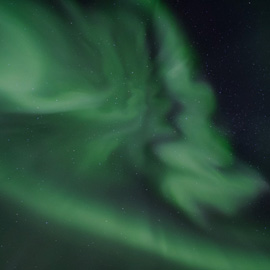 Grün-violette Polarlichter leuchten über verschneiten Hügeln in der skandinavischen Nacht, klarer Sternenhimmel im Hintergrund.