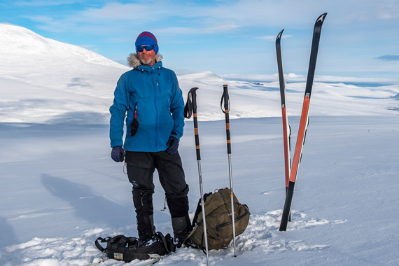 Ein Mann, Mark Renker von Wildtreks steht mit Tourenski, Stöcken und Pulka-Schlitten auf verschneiter Hochebene im Fjell, im Hintergrund sanfte Hügel unter blauem Himmel.